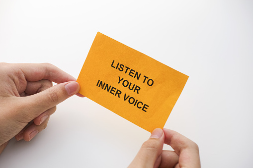 A man holding a yellow paper note with the phrase Listen to your inner voice on it in his hands. Close up.