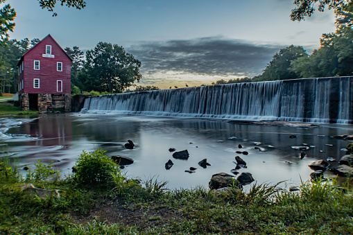 Sunrise at Starr's Mill Georgia historic landmark in Fayette County with manmade waterfall and red mill barn with dramatic sky