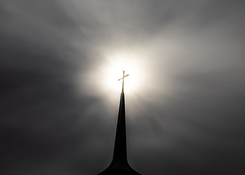 Back lit church steeple with sun directly behind Christian cross illuminating symbol of faith