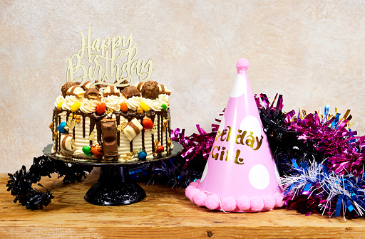birthday girl party concept, layer Cake with happy birthday test and colorful tinsel on wood table