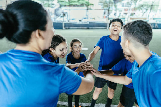 A group of cheerful kids and their trainer gather closely on a sunny soccer field, expressing team spirit and friendship. Perfect for illustrating teamwork and sportsmanship in youth activities.