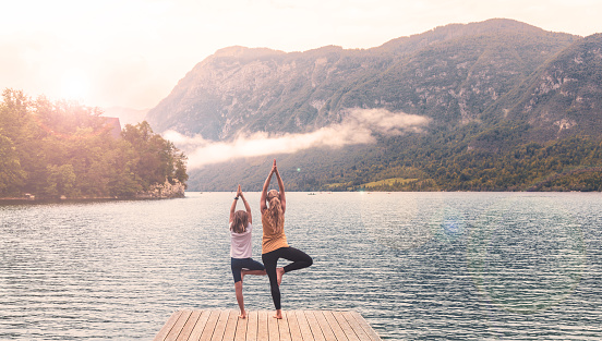 Mother and child doing yoga on pier in front of beautiful lake- Bohinj lake in Slovenia