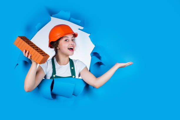 istock building a house. Kid build construction. engineer teen is construction worker. Professional craftsman or workman. International workers day. girl in helmet of builder with brick. presenting product 1695801398