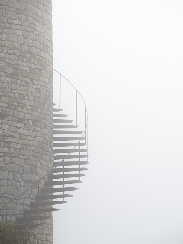 Part of an old stone tower with an exterior staircase on a foggy day.