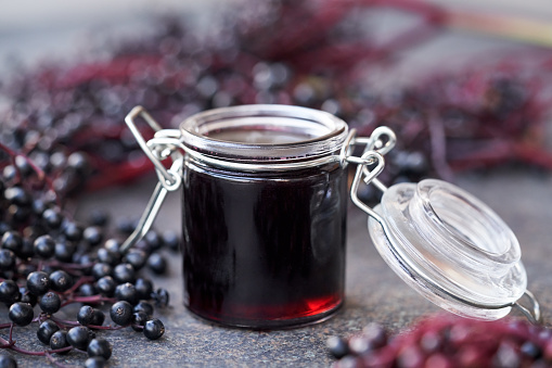 A jar of black elderberry syrup with fresh berries on dark background