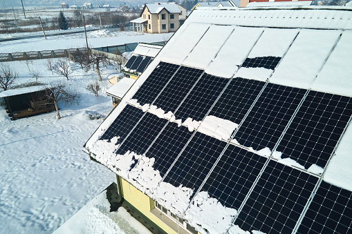 Aerial view of snow melting from covered solar photovoltaic panels installed on house rooftop for producing clean electrical energy. Low effectivity of renewable electricity in nothern region winter.