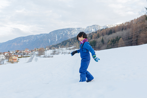 side view on girl going down on snow slope in colorful winter clothes against mountain backdrop