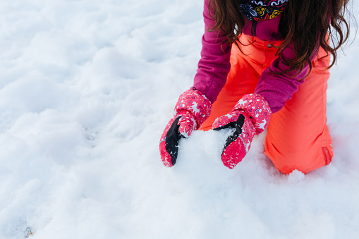 close up on hands in gloves of the girl in orange pants playing with snow