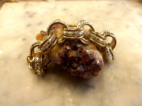 Gold and silver chain bracelet draped over a chunk of amethyst sitting on marble.