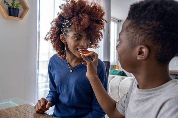 istock Afro-Latino mother and son chat and eat at the dining table while watching videos on cell phone. 1695961074