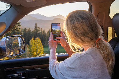 She takes photo across the forest to the sunrise over mountains distant, Crowsnest Pass, Alberta