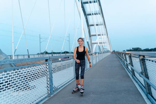 With the city as her backdrop, a young woman enjoys the briskness of the air as she smoothly maneuvers her roller skates across the bridge, portraying a sense of freedom and joy