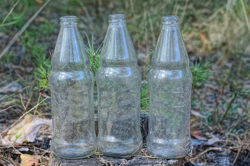 three white old dirty glass bottles stand on the gray ground in the street