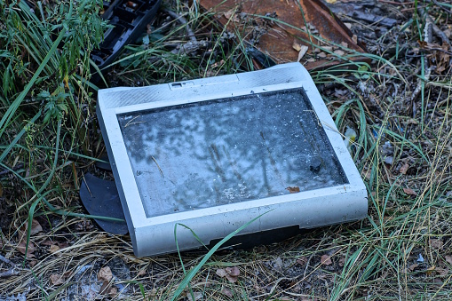 garbage from one old gray square TV lies on the ground and in the green grass on the street