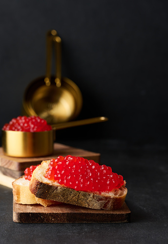 Red caviar on slices of white wheat bread on a black table, concept of luxury and gourmet cuisine