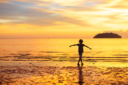 Child playing on ocean beach. Kid jumping in the waves at sunset. Sea vacation for family. Little boy running on exotic island during summer holiday.