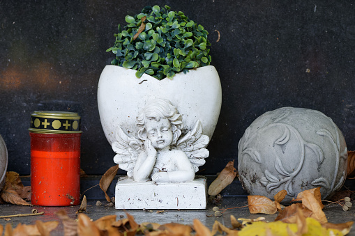 autumn foliage lies on a grave decoration with grave light and a flower vase with angel figure