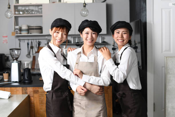 Several smiling young Asian women in aprons working cheerfully at a restaurant