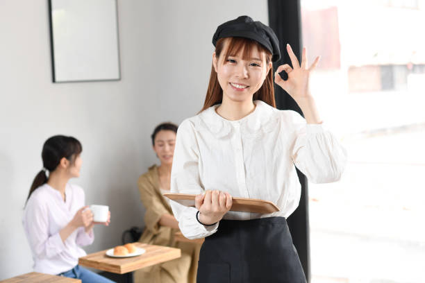 앞치마를 입고 웃고 있는 젊은 아시아 여성이 식당에서 즐겁게 일하라는 ok 신호를 보냅니다. - soda jerk 뉴스 사진 이미지