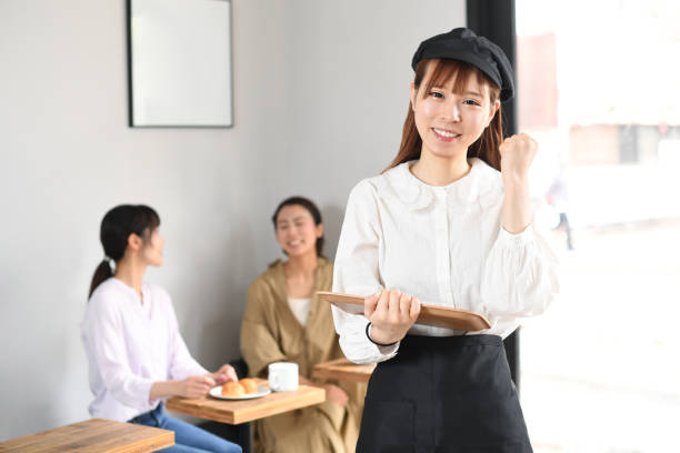 a smiling young asian woman in an apron doing a fist pump while working cheerfully at a restaurant - soda jerk imagens e fotografias de stock