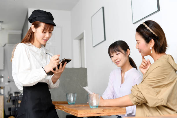 앞치마를 입은 웃고 있는 젊은 아시아 여성이 레스토랑에서 유쾌하게 손님을 접대하고 주문을 하는 손님 - soda jerk 뉴스 사진 이미지