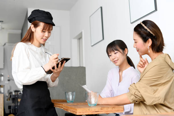 a smiling young asian woman in an apron cheerfully serving customers at a restaurant and a customer placing an order - soda jerk imagens e fotografias de stock