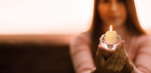 Young girl in blur holding a lit candle in close-up. In a dark environment. Space for text.