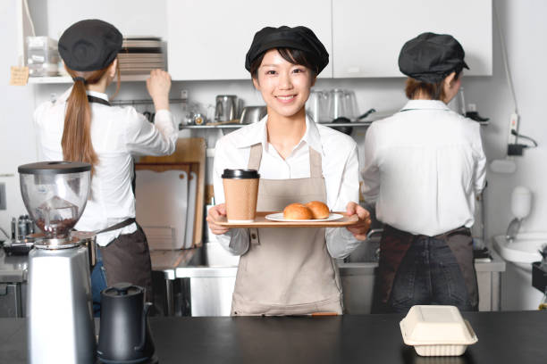 a young asian woman serving customers with a smile at the kitchen counter of a restaurant and young female staff working in the kitchen. - soda jerk imagens e fotografias de stock