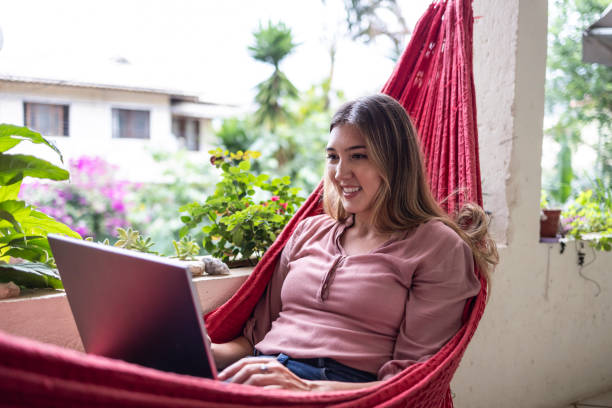 istock Latina woman using laptop lying in hammock at home 1696182547
