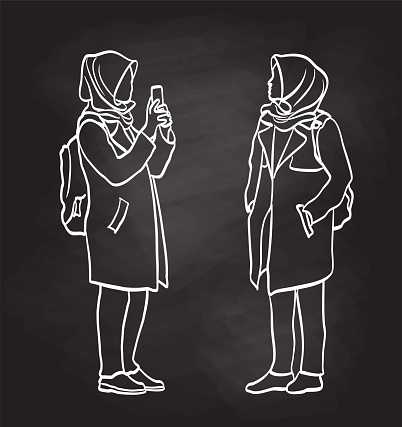 Two views of a woman wearing a hijab, one where she is standing with her hands in her pockets and another holding her phone and taking a picture