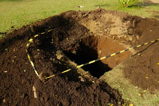 Photo of The soil is excavated in grass field so that it leaves a gaping hole