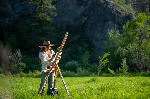 Female artist painting with an easel outdoors. Creative people with a unique process.