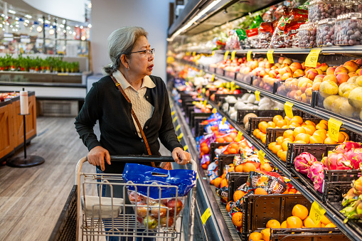 High quality stock photo of an authentic Asian-American Filipino senior woman shopping for food at a local grocery store, coping with high prices as inflation continues to push deeper into fixed incomes.