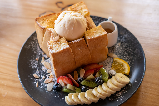 Honey toast, a Japanese dessert served with ice cream and blueberry, strawberry, banana and honey on plate
