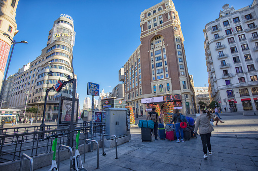 View of Gran Via street in the morning, Madrid, Spain. Tourists with suitcases near Callao Metro Station.