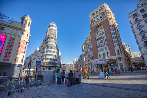 View of Gran Via street in the morning, Madrid, Spain. Tourists with suitcases near Callao Metro Station.