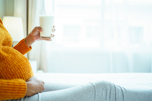 Happy African - American black pregnant woman relaxing - lying down on the bed and holding a glass of fresh milk. Essential nutrition for pregnancy woman. Pregnant woman drinks a milk.