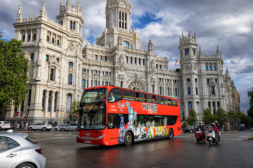 Street view of Palace of Communication on the Plaza de Cibeles in Madrid, Spain. A tourbus and 3 motorcycles passing by.