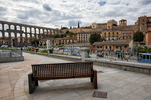 Street view of the Roman Aqueduct, Segovia, Spain. An iron bench in the sidewalk.