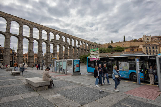 Street view of the Roman Aqueduct, Segovia, Spain. Tourists and a bus at bus stop.