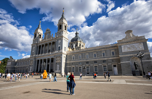 Exterior view of Almudena Cathedral on a sunny afternoon, Madrid, Spain. Many tourists at the Plaza de Armeria can be seen.