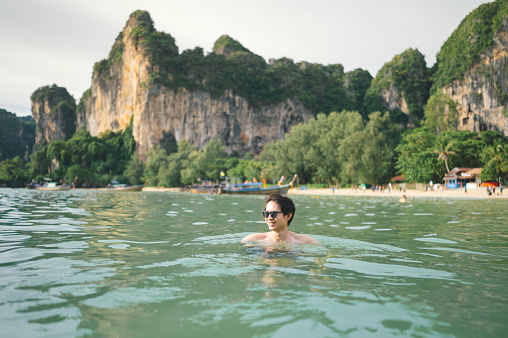 Wide view Portrait of young solo tourist floating in the emerald sea and relaxing on summer vacations at railay island in background thailand