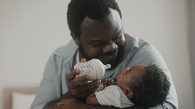 African father carry and feeding milk from bottle to his little infant baby boy at home.