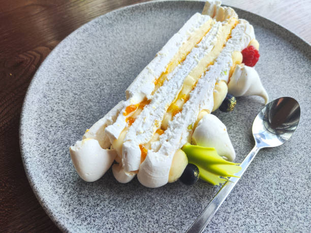 istock Pavlova cake on a wooden table in restaurant. This is a meringue-based multilayerd dessert with cream inside. Served with napkin on a grey granite plate 1696559902