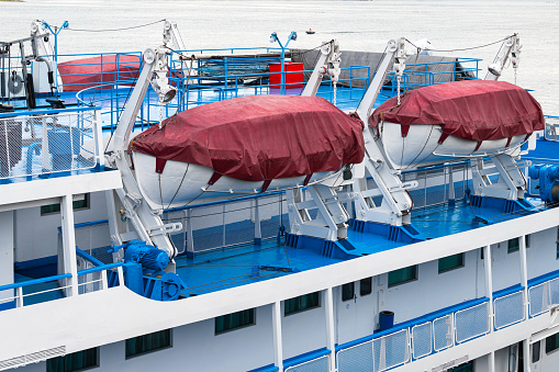 lifeboats on board the ship. the boats are secured with rigging devices and covered with burgundy awnings