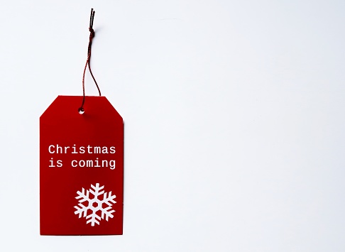 Red gift tag with written text CHRISTMAS IS COMING, concept of start planning for Christmas New Year Holiday celebration which is coming soon