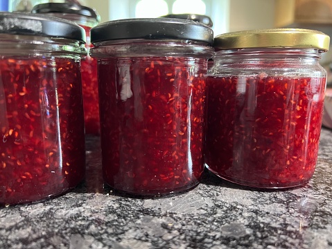Freshly made raspberry jam has been poured into jam jars