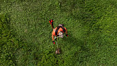 Aerial view of worker in protective clothing cutting grass with brushcutter