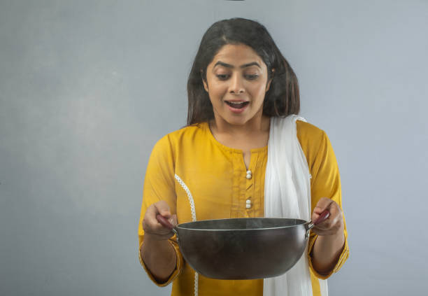 istock Woman holding cooking pan while standing over white background 1696633387