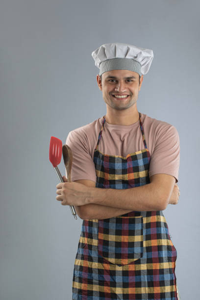 istock Male chef with spoon and spatula standing on white background 1696645554